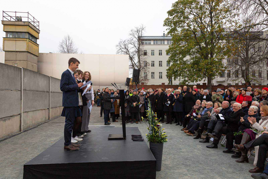 Schülerinnen und Schüler stehen auf einer Bühne vor der Hinterlandmauer und halten Reden. Das Publikum mit Bundespräsident Steinmeier steht und sitzt im Halbkreis um die Bühne.